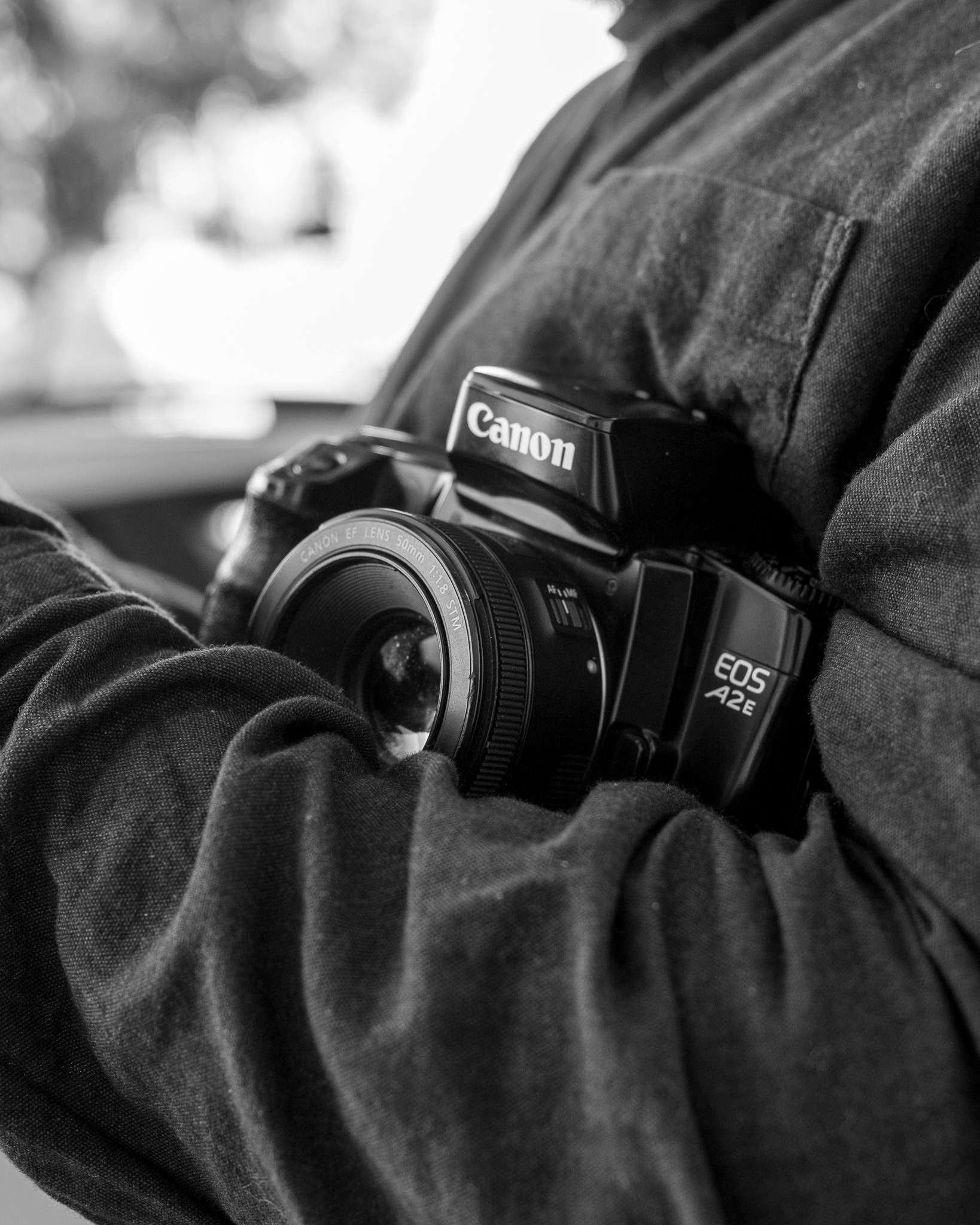An old Canon EOS film camera held close against a dark shirt, in black and white