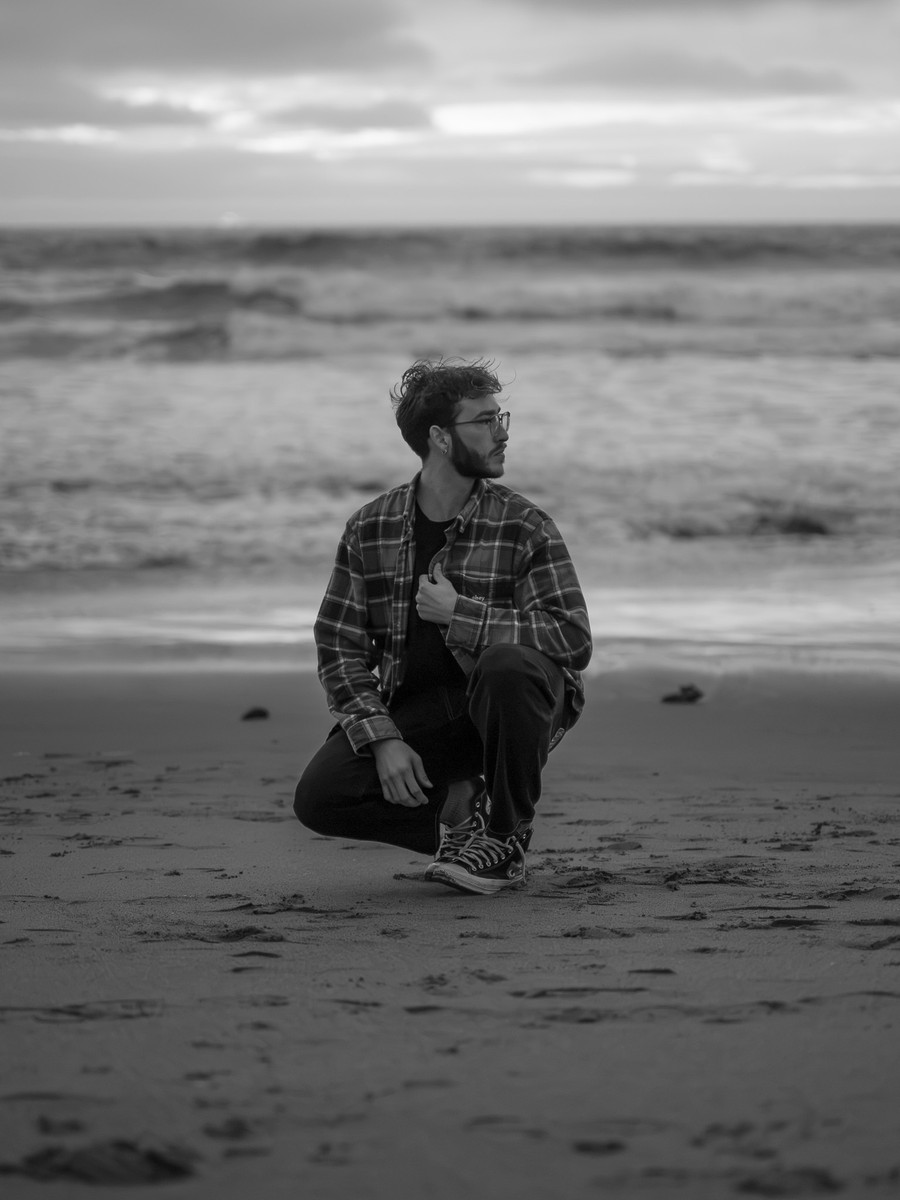 David Virin crouching on the beach in black and white, looking out to sea